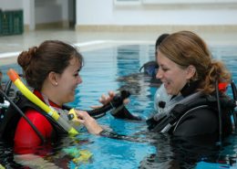 Instructor show Student how to inflate the BCD in the pool